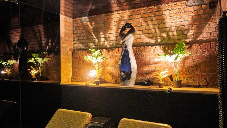 Decorative alcove featuring tall abstract statue flanked by small lamps and foliage.
