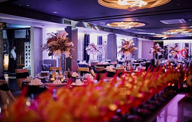 Lavishly decorated reception space bathed in purple light, tables dressed, waiter visible.