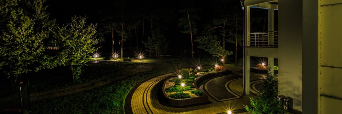 Podświetlona nocą ścieżka wzdłuż nowoczesnego budynku hotelowego otoczona zielenią i delikatnym oświetleniem ogrodowym