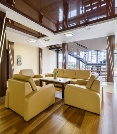 Nowoczesny hotelowy salon z jasnobeżowymi skórzanymi sofami, dużą stolik kawowy, drewnianą podłogą i szklanymi drzwiami na taras