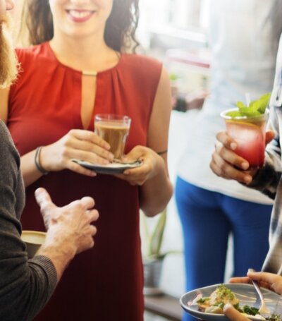 Grupa gości rozmawia przy hotelowym bufecie, pijąc kawę, koktajle i jedząc przekąski w jasnej przestrzeni