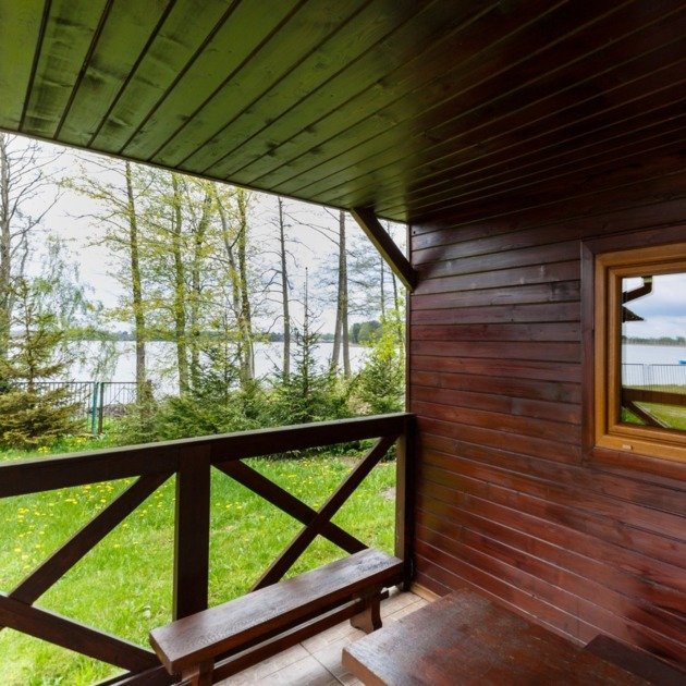 Drewniany taras domku letniskowego z ławką, widokiem na jezioro i otaczającą zieleń w spokojnej, naturalnej scenerii