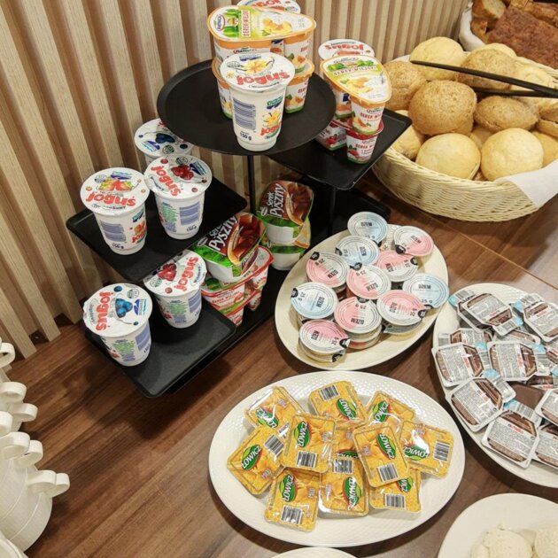 Śniadaniowy bufet z jogurtami, serkami, dżemami, masłem oraz świeżym pieczywem w koszu na drewnianym stole.