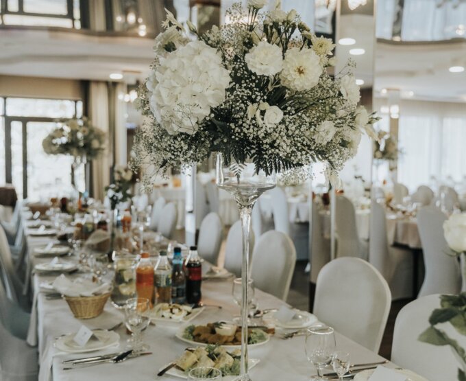 Elegancko udekorowana sala bankietowa z białymi kwiatami na wysokich wazonach i zastawą stołową na uroczysty obiad