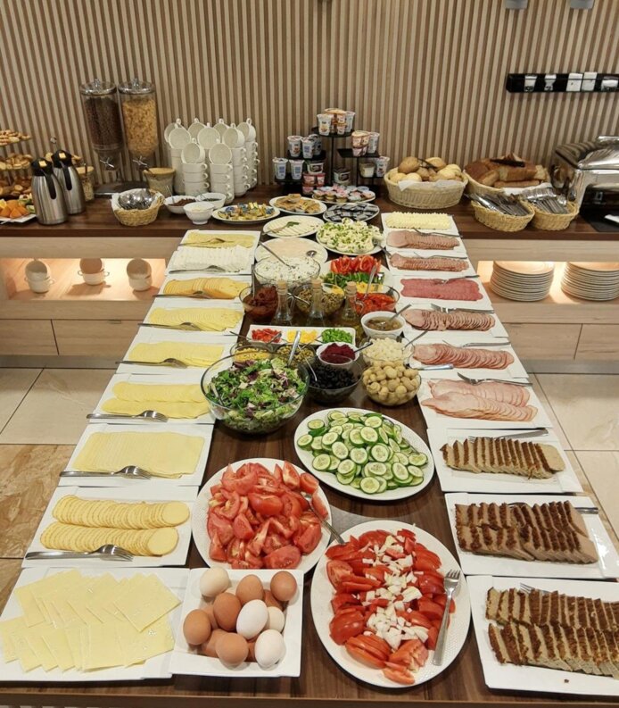 Bufet śniadaniowy z różnorodnymi serami, wędlinami, świeżymi warzywami, jajkami, pieczywem i sałatkami w nowoczesnym wnętrzu