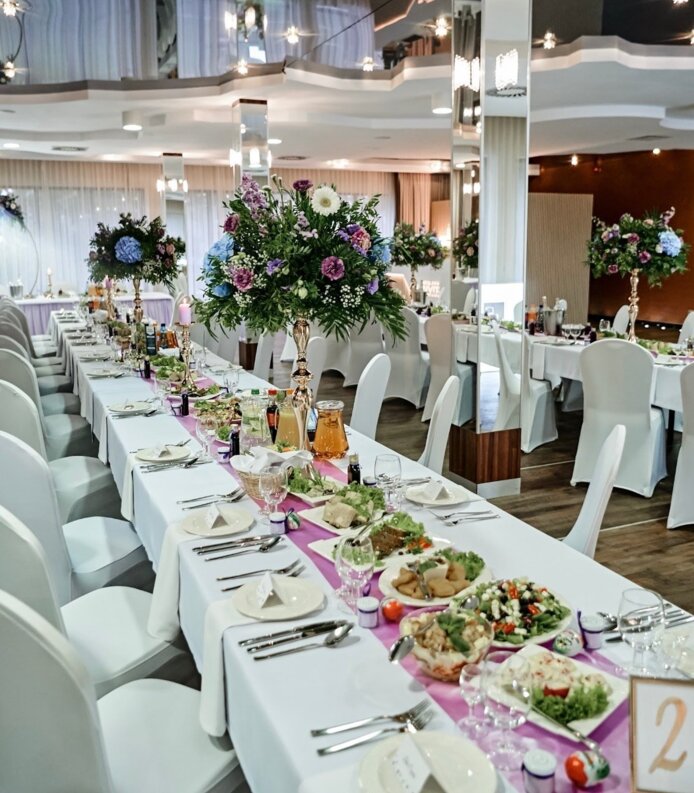 Elegancko udekorowana sala bankietowa z białymi obrusem, bukietami kwiatów i wykwintnym nakryciem stołu na uroczystą kolację