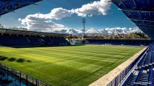 Football stadium with freshly mowed pitch and empty stands under clear sky with mountain backdrop