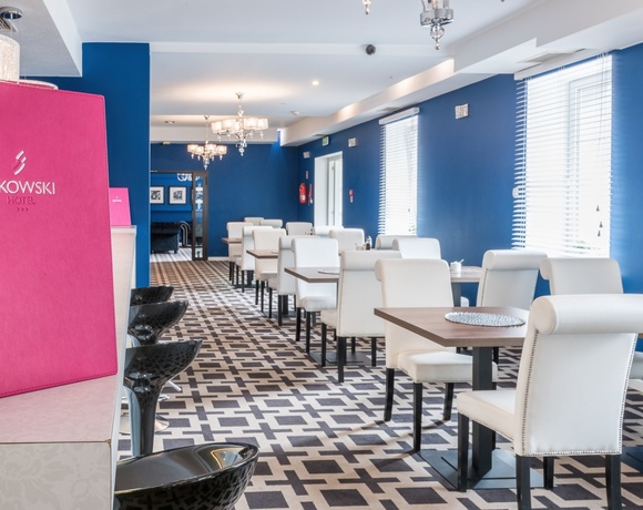 Stylowa jadalnia hotelowa z niebieskimi ścianami, białymi tapicerowanymi krzesłami, drewnianymi stołami i różowym menu