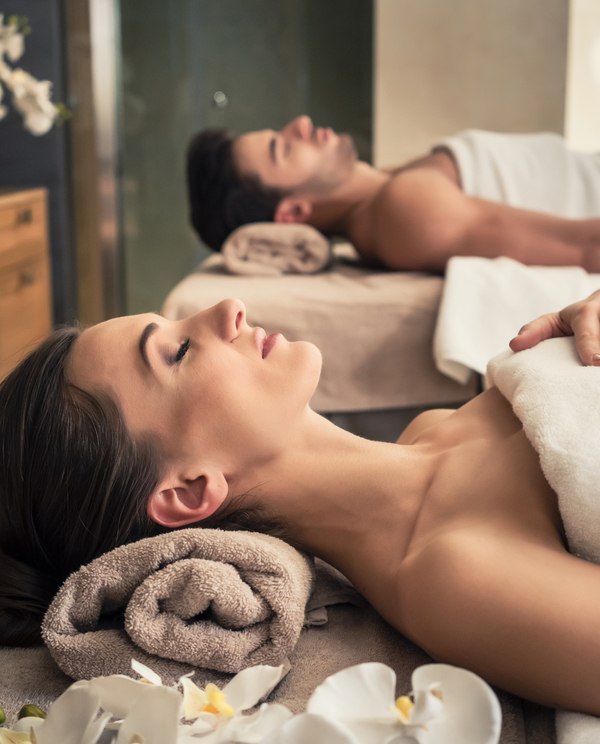 Para w spa podczas relaksacyjnego masażu — leżanki z ręcznikami, płonące świece, storczyki i kojący nastrój.