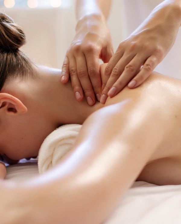 Kobieta otrzymująca masaż karku i pleców w spokojnym spa; dłonie terapeuty, ręcznik pod głową, miękkie światło i relaksująca atmosfera