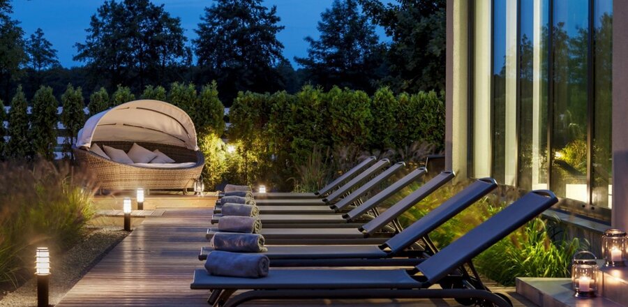 Taras spa hotelu o zmierzchu — rząd leżaków z zwiniętymi ręcznikami, nastrojowe lampy i pleciony szezlong z baldachimem