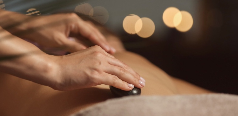 Gorący kamień na plecach podczas relaksującego masażu w spa; delikatne dłonie terapeuty, ciepłe, przytłumione światło.
