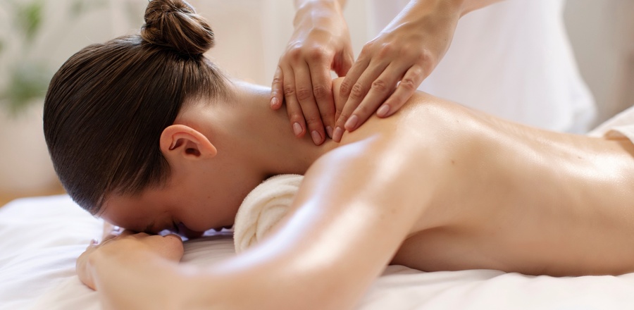 Kobieta otrzymująca masaż karku i pleców w spokojnym spa; dłonie terapeuty, ręcznik pod głową, miękkie światło i relaksująca atmosfera