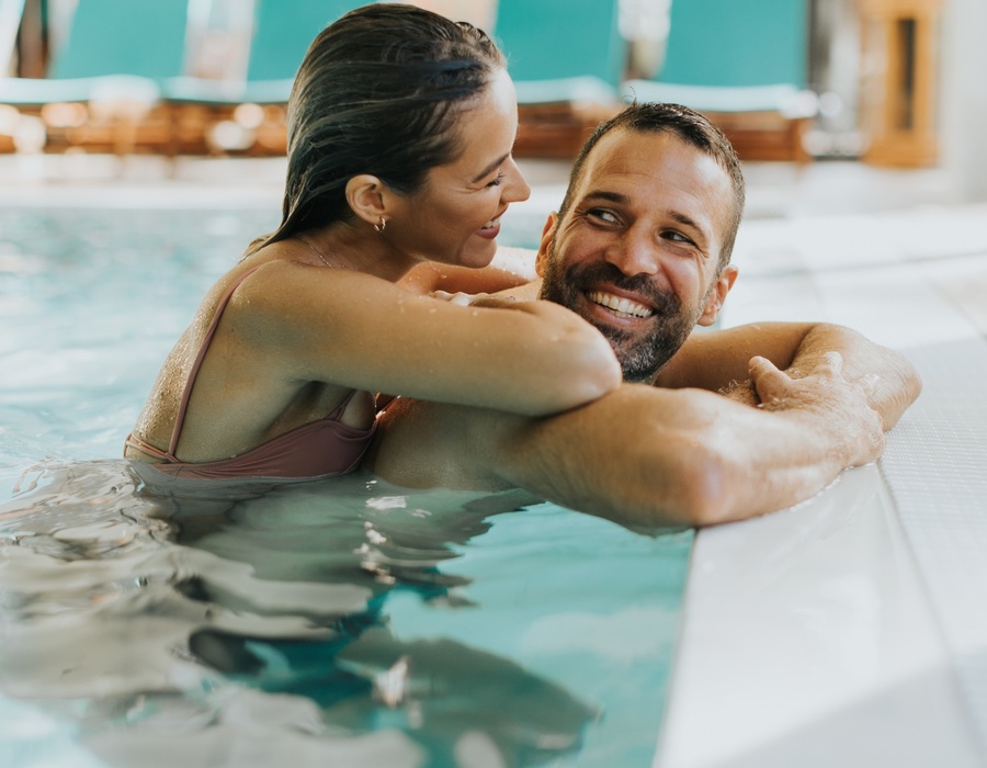 Para relaksuje w hotelowym basenie wewnętrznym przy krawędzi, uśmiechy i romantyczna, odprężająca atmosfera