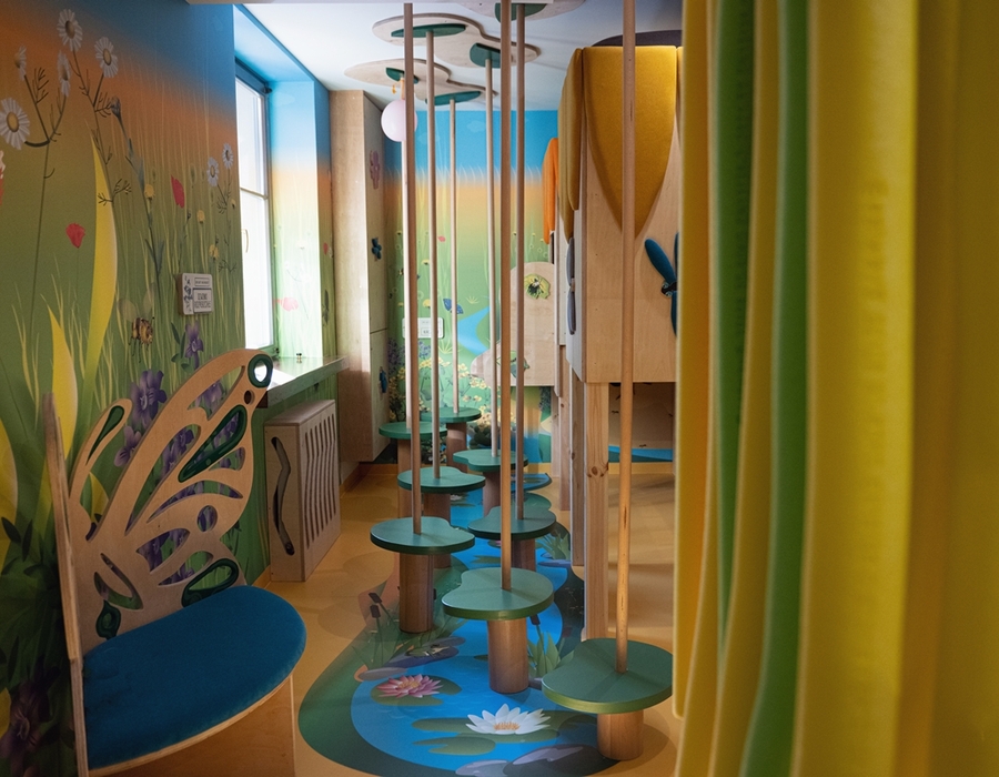 Kolorowy hotelowy klub dziecięcy z leśnym muralem, motylkową ławką, platformami do wspinaczki i prywatnymi zasłonami.