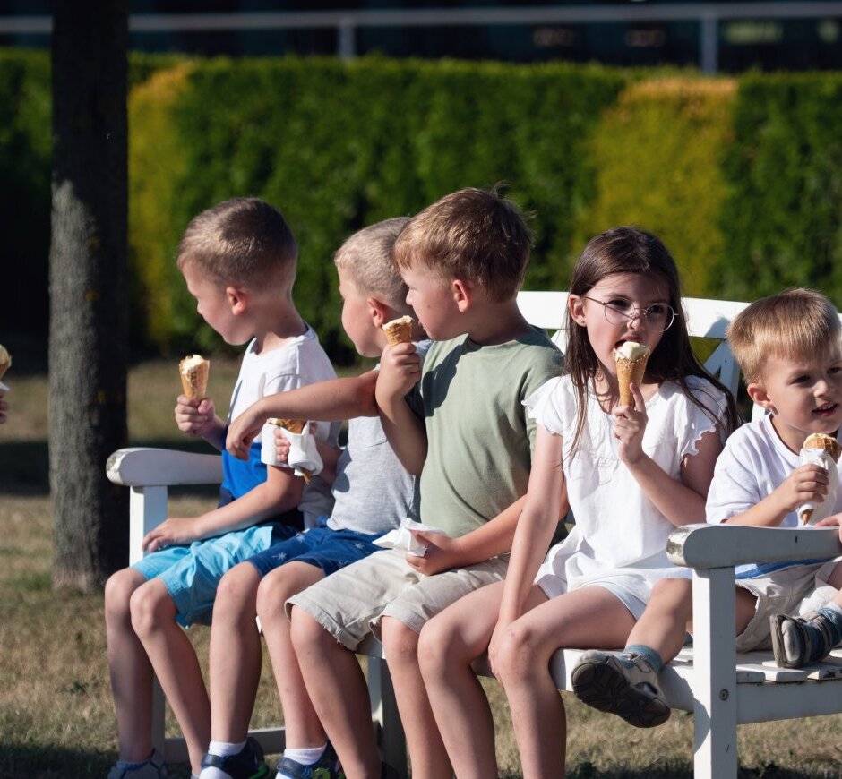 Kilka dzieci jedzących lody na białej ławce w słonecznym, zielonym ogrodzie – przyjazne miejsce dla rodzin.