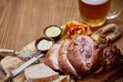 Scheiben von gebratenem Schweinshaxenfleisch, serviert auf einem Holzbrett mit frischem Brot, Senf, Meerrettich und eingelegter Paprika, dazu ein halber Liter frisch gezapftes Bier aus der Familienbrauerei Morous. Eine traditionelle tschechische Spezialität, serviert im Restaurant des Hotels Slunce in Rýmařov im Altvatergebirge (Jeseníky).