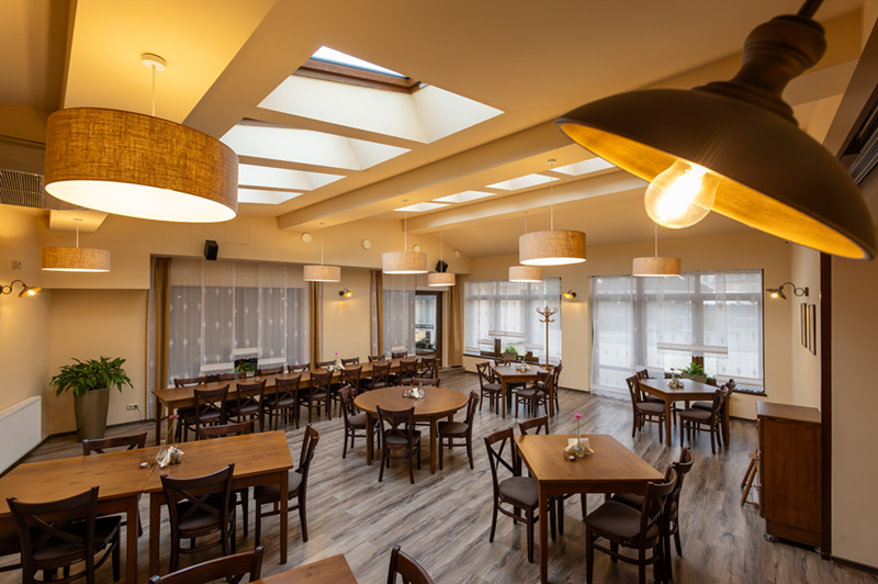 Příjemná hotelová jídelna se střešními okny, dřevěnými stoly a židlemi, závěsnými lampami a květinami na stole k snídani.