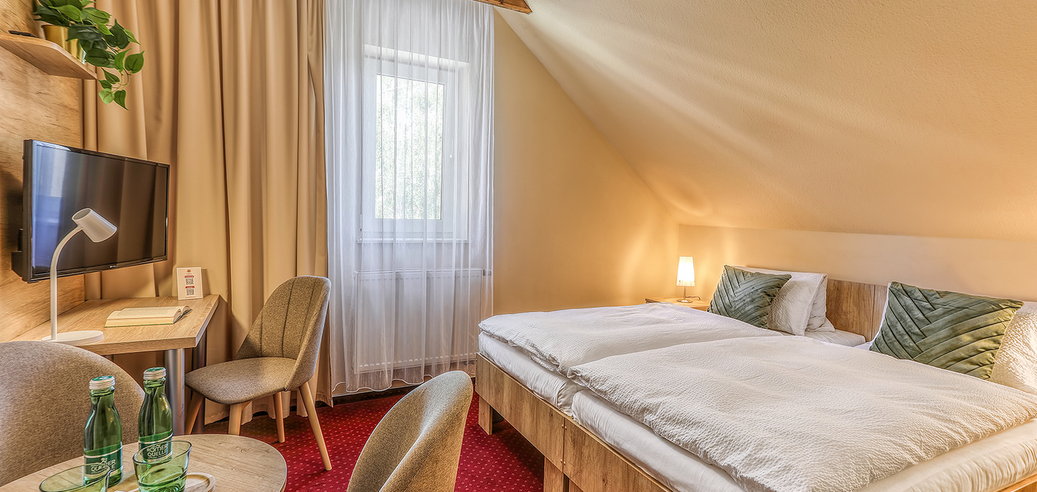Příjemný dvoulůžkový pokoj v Hotelu Slunce Rýmařov v Jeseníkách s dřevěnými trámy, TV, psacím stolem a pohodlným posezením.