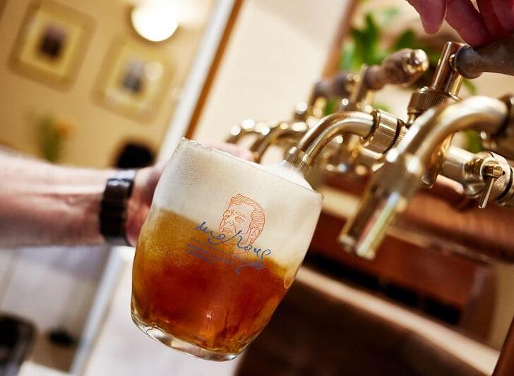 Barman plní značkový půllitr pěnivým jantarovým točeným pivem z leštěných mosazných kohoutů