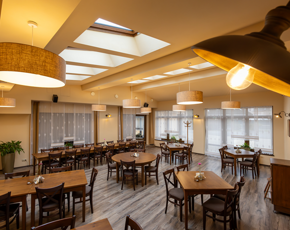 Příjemná hotelová jídelna se střešními okny, dřevěnými stoly a židlemi, závěsnými lampami a květinami na stole k snídani.