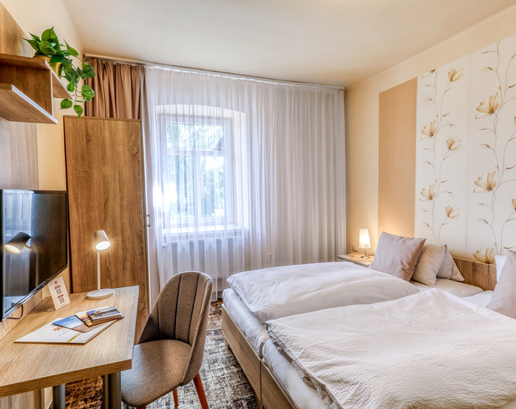 Světlý pokoj s oddělenými lůžky v Hotelu Slunce Rýmařov v Jeseníkách, měkkým povlečením, pracovním stolem, TV a útulnou atmosférou.