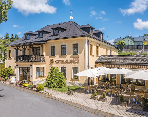 Budova Hotelu Slunce Rýmařov v Jeseníkách s balkonem, venkovní terasou se slunečníky a upraveným vstupem.