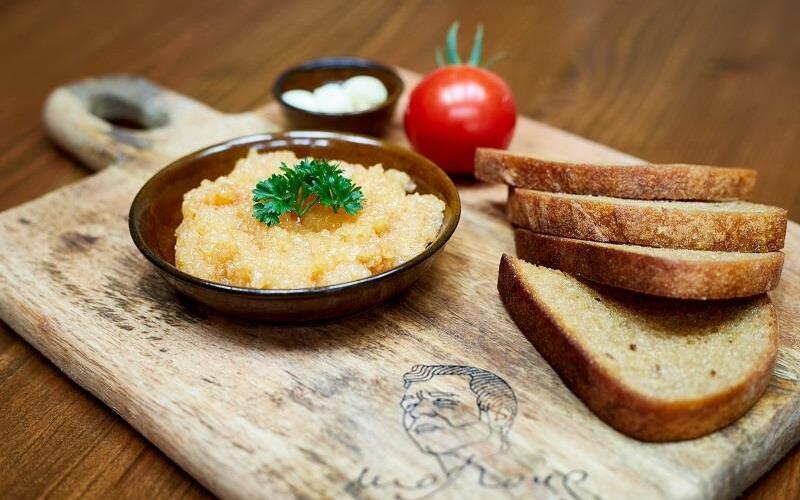 Rustikales Holzbrett mit einer Schale würzigen Aufstrichs, Petersilie, gerösteten Brotscheiben, Cocktailtomate und Butter.