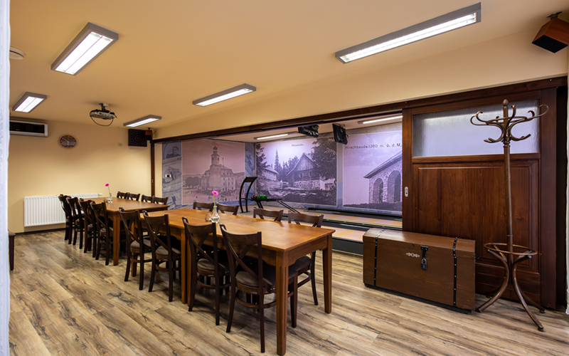 Gemütlicher Hotel-Konferenz- und Speiseraum mit langen Holztischen, Stühlen, Deckenprojektor und historischem Wandbild.