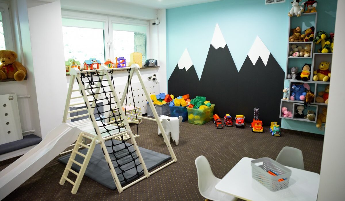 Przytulny hotelowy kącik zabaw: zjeżdżalnia i ścianka do wspinaczki, stolik z krzesełkami, kosze klocków i pluszaki