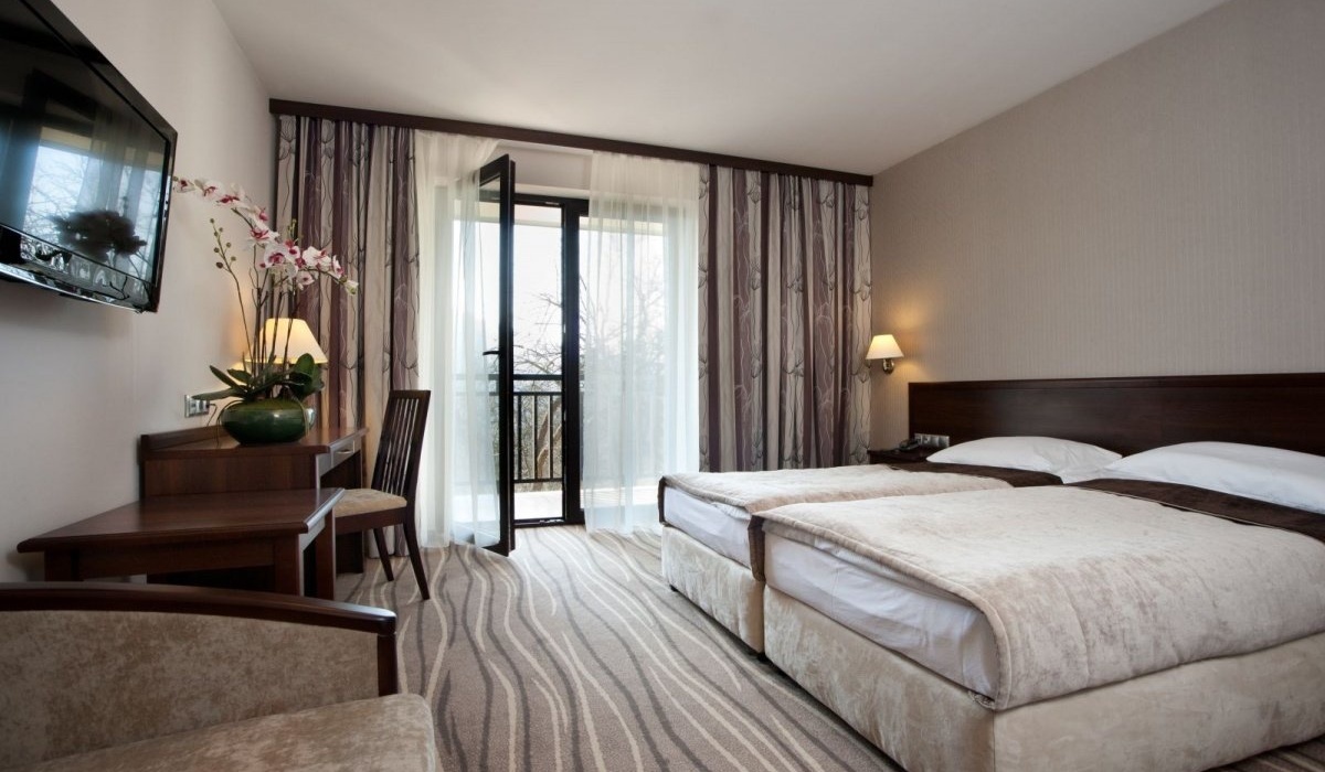 Przytulny pokój z dwoma pojedynczymi łóżkami, francuskim balkonem, biurkiem, telewizorem, lampami i orchideą