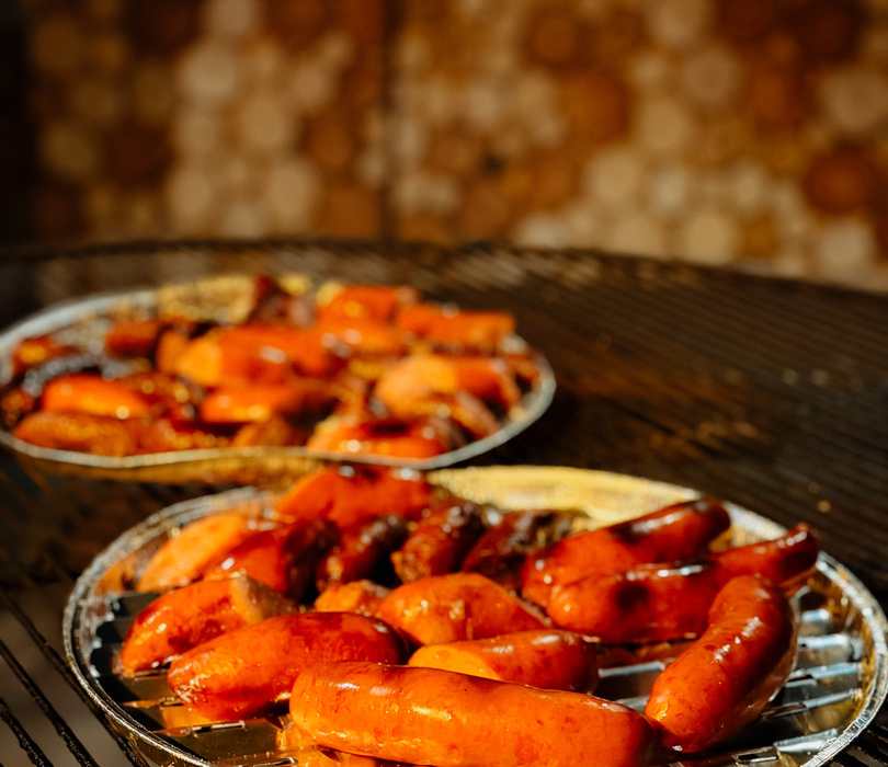 Soczyste, szkliwione kiełbaski na aluminiowych tackach pieczone na ruszcie, ciepłe pomarańczowo-złote oświetlenie