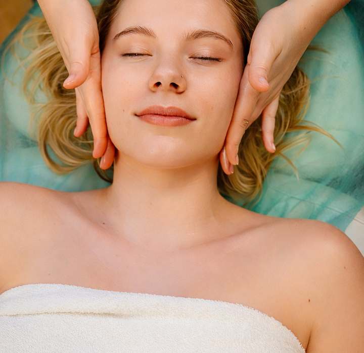 Kobieta z zamkniętymi oczami podczas relaksującego masażu twarzy w pokoju spa, na leżance z białym ręcznikiem