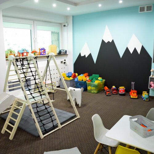 Przytulny hotelowy kącik zabaw: zjeżdżalnia i ścianka do wspinaczki, stolik z krzesełkami, kosze klocków i pluszaki