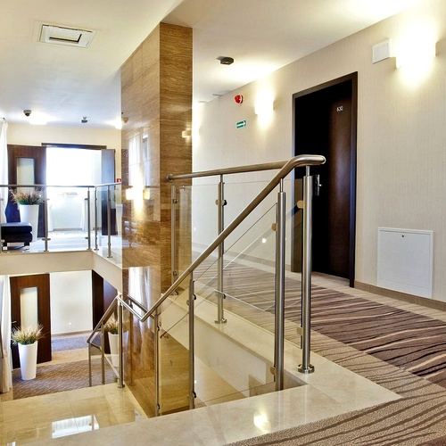 Nowoczesny hotelowy korytarz z dywanem, szklanym balustradami przy schodach, dekoracyjnymi donicami i drzwiami pokoi.