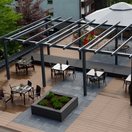 Taras na dachu z pergolą, drewnianą podłogą, stolikami i krzesłami z kwiatami, dużym parasolem i delikatnym oświetleniem