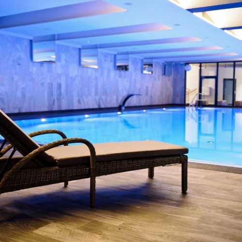 Leżak przy krytym basenie spa hotelowego, niebieskie nastrojowe oświetlenie, nowoczesne płytki i relaksująca atmosfera