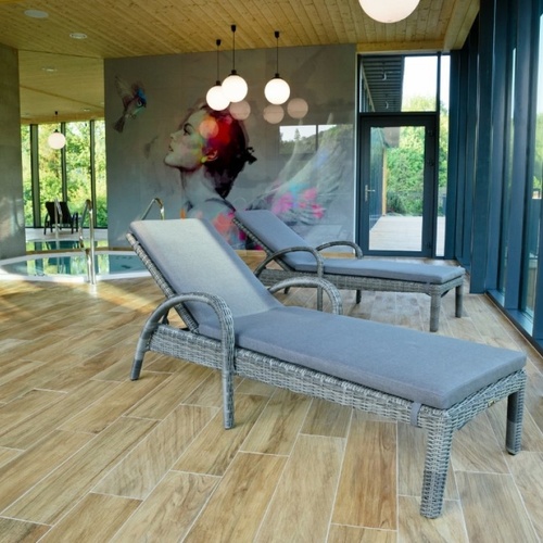 Strefa SPA z dwiema rattanowymi leżankami obok małego basenu, dużymi oknami, muralem i ciepłym drewnianym wykończeniem.