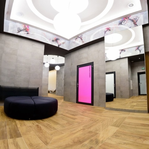 Nowoczesna strefa spa z drewnianą podłogą, okrągłą czarną kanapą, lustrami i widoczną, rozświetloną sauną po prawej.