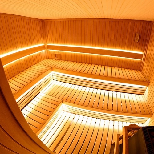 Przestronna drewniana sauna hotelowa z wielopoziomowymi ławkami, podświetleniem LED i piecem z kamieniami
