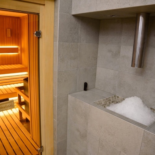 Sauna z drewnianymi ławami i ciepłym podświetleniem oraz przylegający pojemnik z kruszonym lodem i stalową rurą