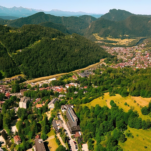 Kompleks hotelowy przy lesistym zboczu i łąkach, miasteczko w dolinie i panoramiczny widok na górskie pasmo