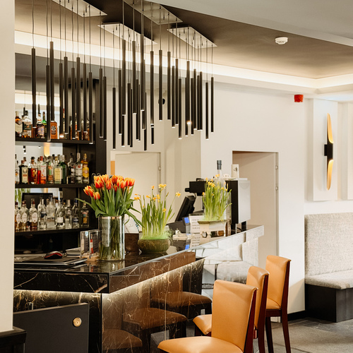 Elegancki bar hotelowy z czarnym marmurowym barem, wiszącymi stalowymi lampami, skórzanymi stołkami i bukietami tulipanów.