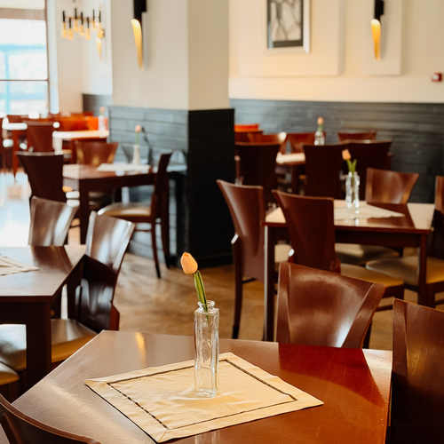 Jasna restauracja hotelowa z drewnianymi stolikami, pojedynczym tulipanem w szklanym wazonie i ciepłym oświetleniem.