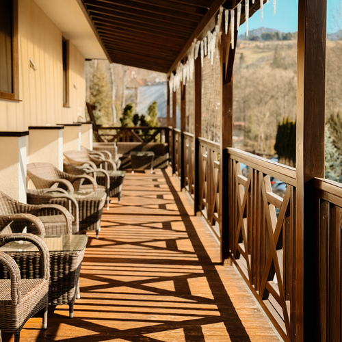 Zadaszony drewniany taras hotelowy z rzędem wiklinowych foteli i stolików, widok na góry, wiszące sopelki lodu.