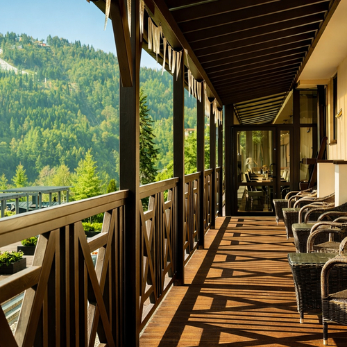 Drewniany hotelowy taras z wiklinowymi fotelami, porannym słońcem i widokiem na zalesione górskie stoki