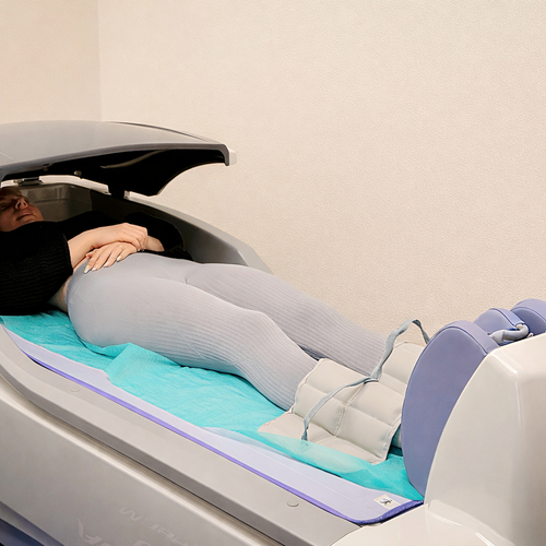 Gość leżący w nowoczesnej kapsule spa z kompresją nóg, miękkim materacem i łagodnym, relaksującym wnętrzem.