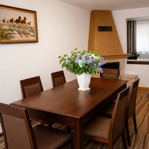 Jadalnia z ciemnym drewnianym stołem i sześcioma krzesłami, wazon z bzem na środku, kominek i obraz z końmi.