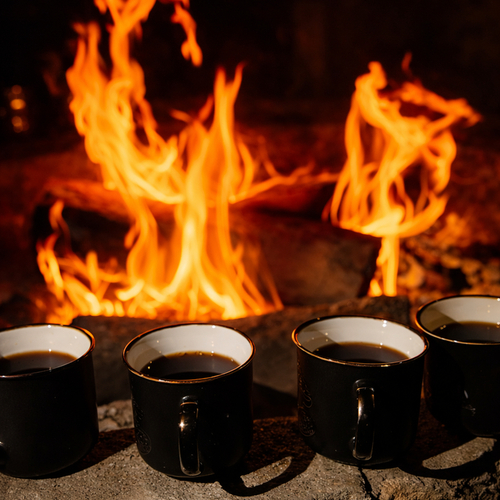 Cztery czarne kubki z gorącym napojem ustawione na kamieniu przed trzaskającym kominkiem, przytulna atmosfera