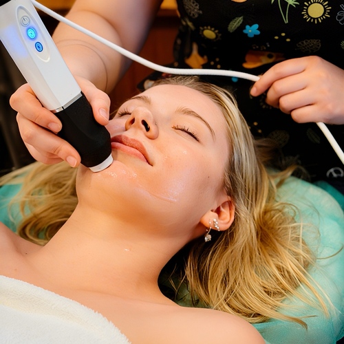 Kobieta relaksuje się podczas zabiegu twarzy w hotelowym spa, kosmetyczka używa urządzenia do oczyszczania i liftingu skóry